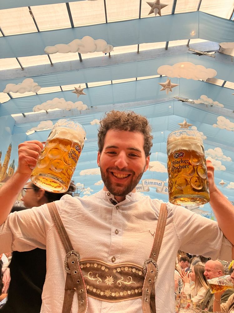 Brandon in lederhosen at Oktoberfest holding two steins