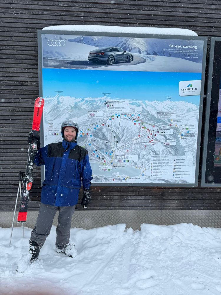Brandon holding skis in the snow in front of a trail map